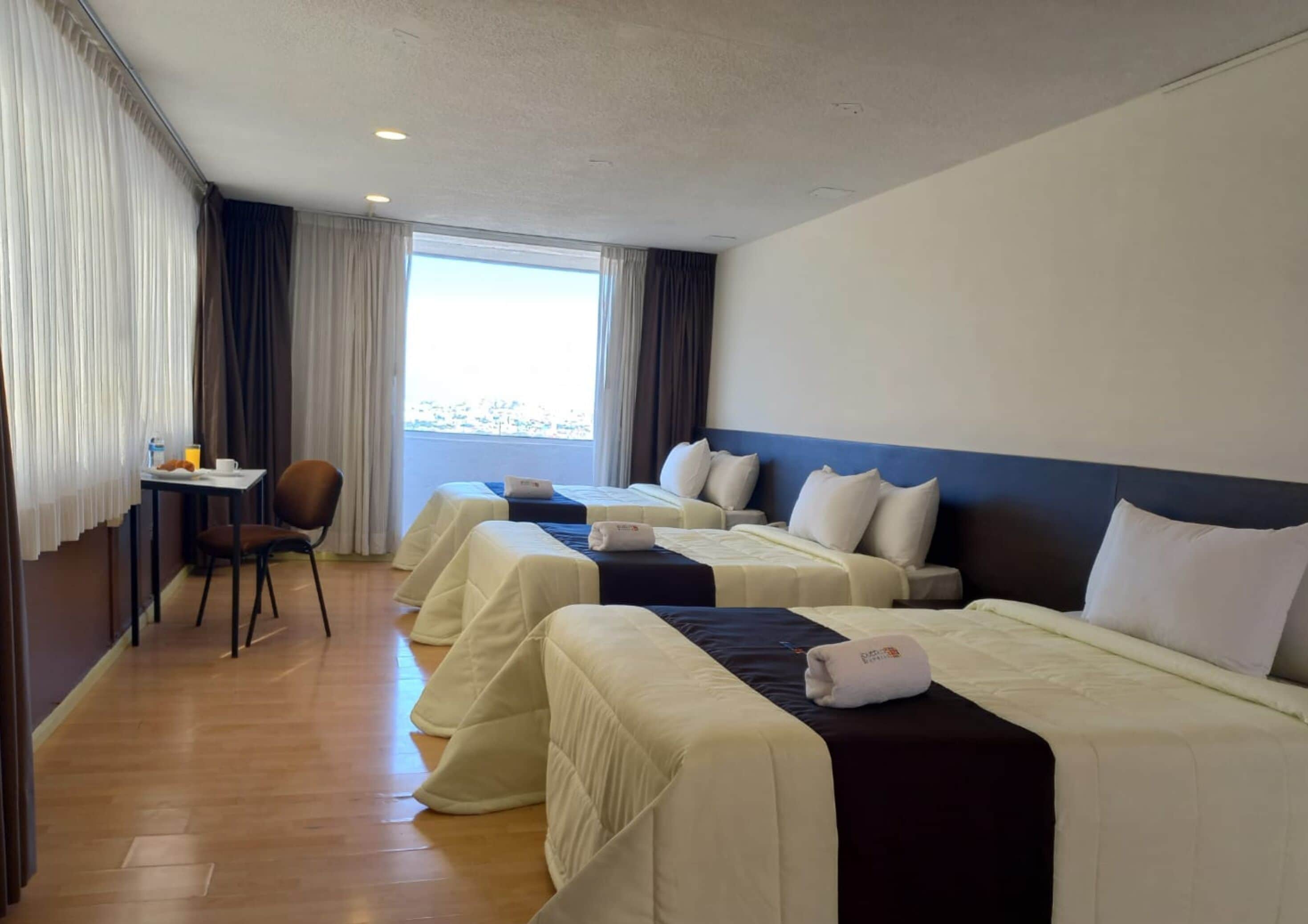A hotel room with two beds, a small table with a chair, and a window with curtains.