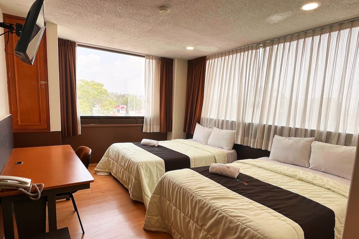 Habitación de hotel con dos camas, un escritorio, una silla y un televisor.