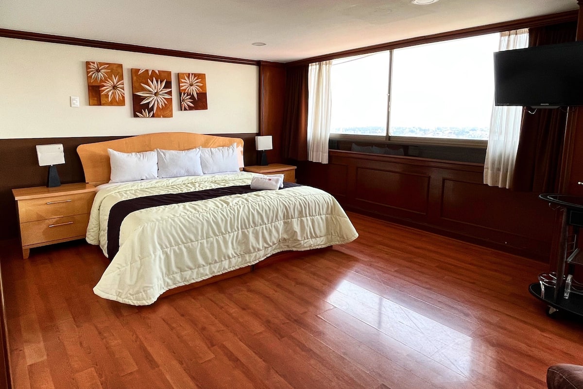 Una habitación de hotel con una cama grande, suelo de madera, televisión y una obra de arte en la pared.
