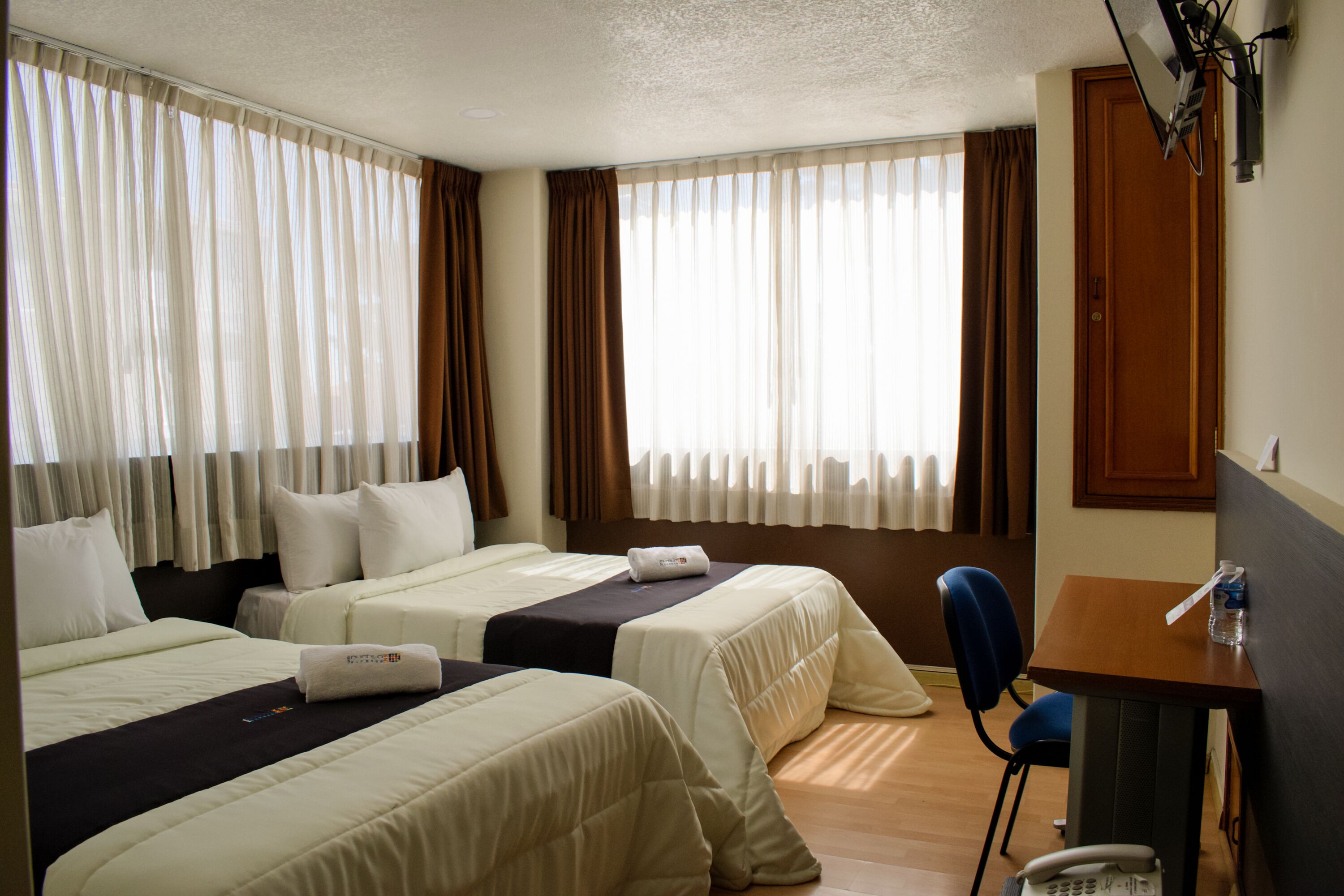 A hotel room with two beds, a desk, and a chair.