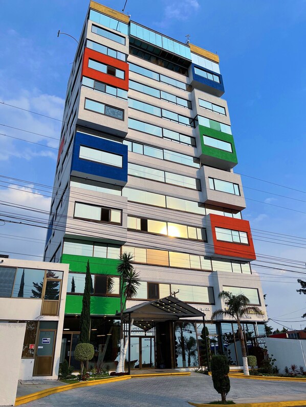 Un hotel de varios pisos con un diseño moderno, que presenta una combinación de paneles de vidrio y superficies sólidas en la fachada.