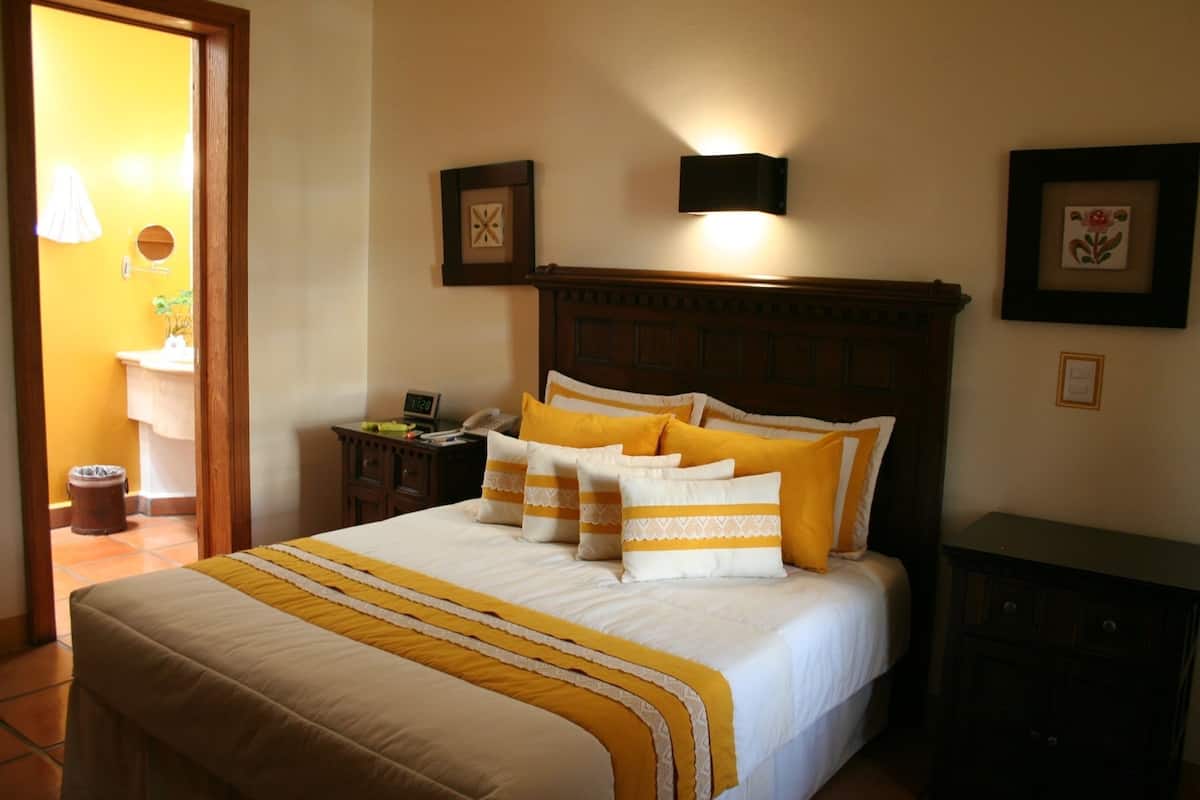 A neatly made bed with a wooden headboard, a bedside table with a lamp, and framed pictures on the wall.