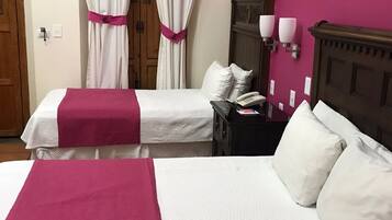 Habitación de hotel con dos camas, un armario de madera, una mesita de noche con un teléfono y una lámpara de pared.