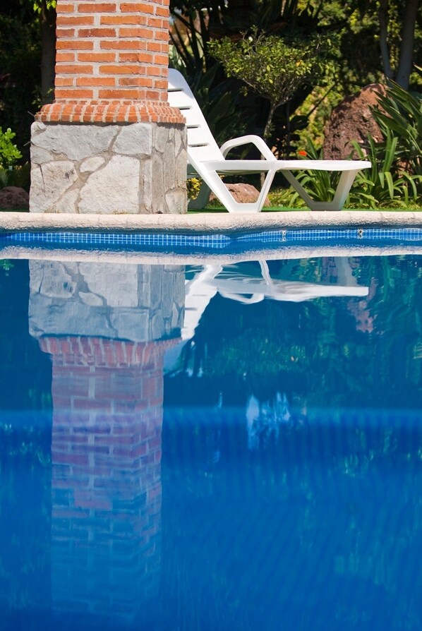 Una piscina azul cristalina con una estructura de ladrillo y sillas de descanso blancas.
