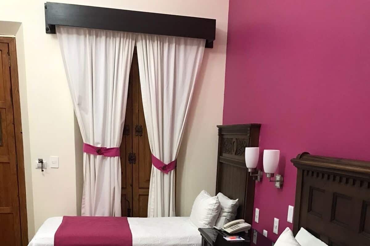 A hotel room with two beds, a wooden wardrobe, a nightstand with a phone, and a wall-mounted lamp.