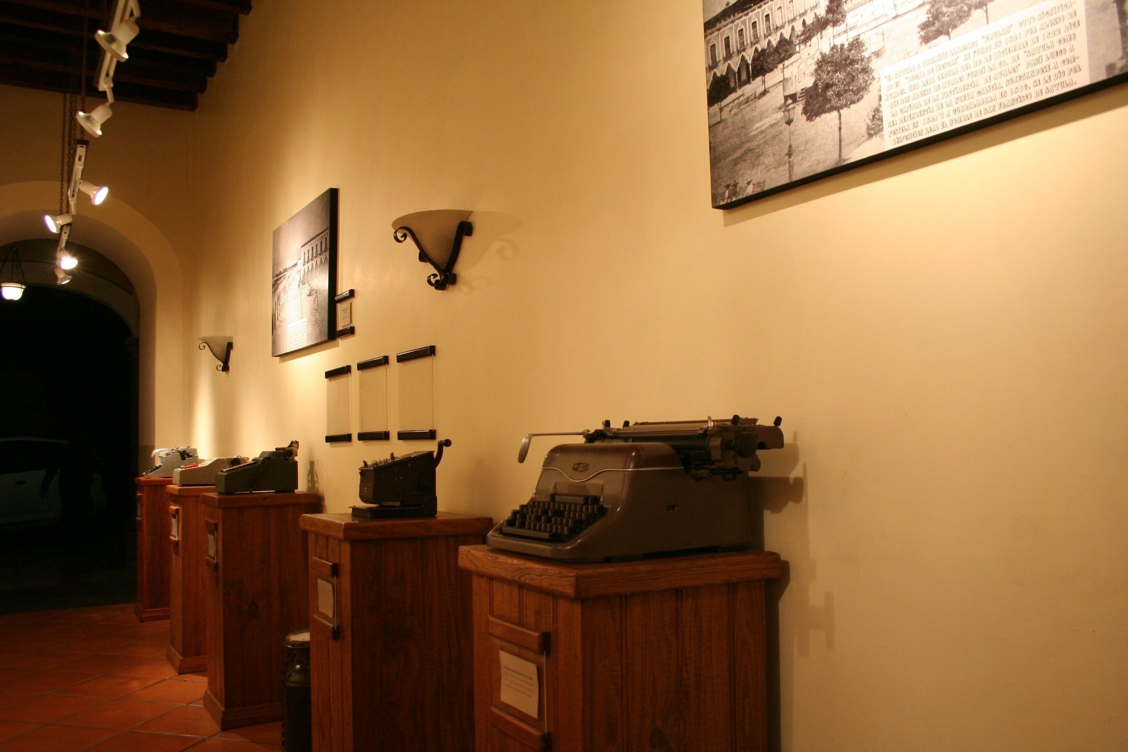 Un pasillo con armarios de madera, una máquina de escribir antigua y lámparas fijadas a la pared.