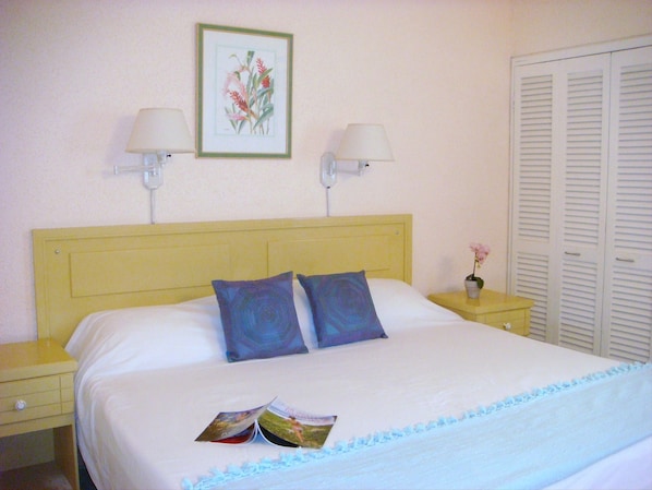 A neatly made bed with two pillows, a bedside table with a lamp, and a framed botanical print on the wall.