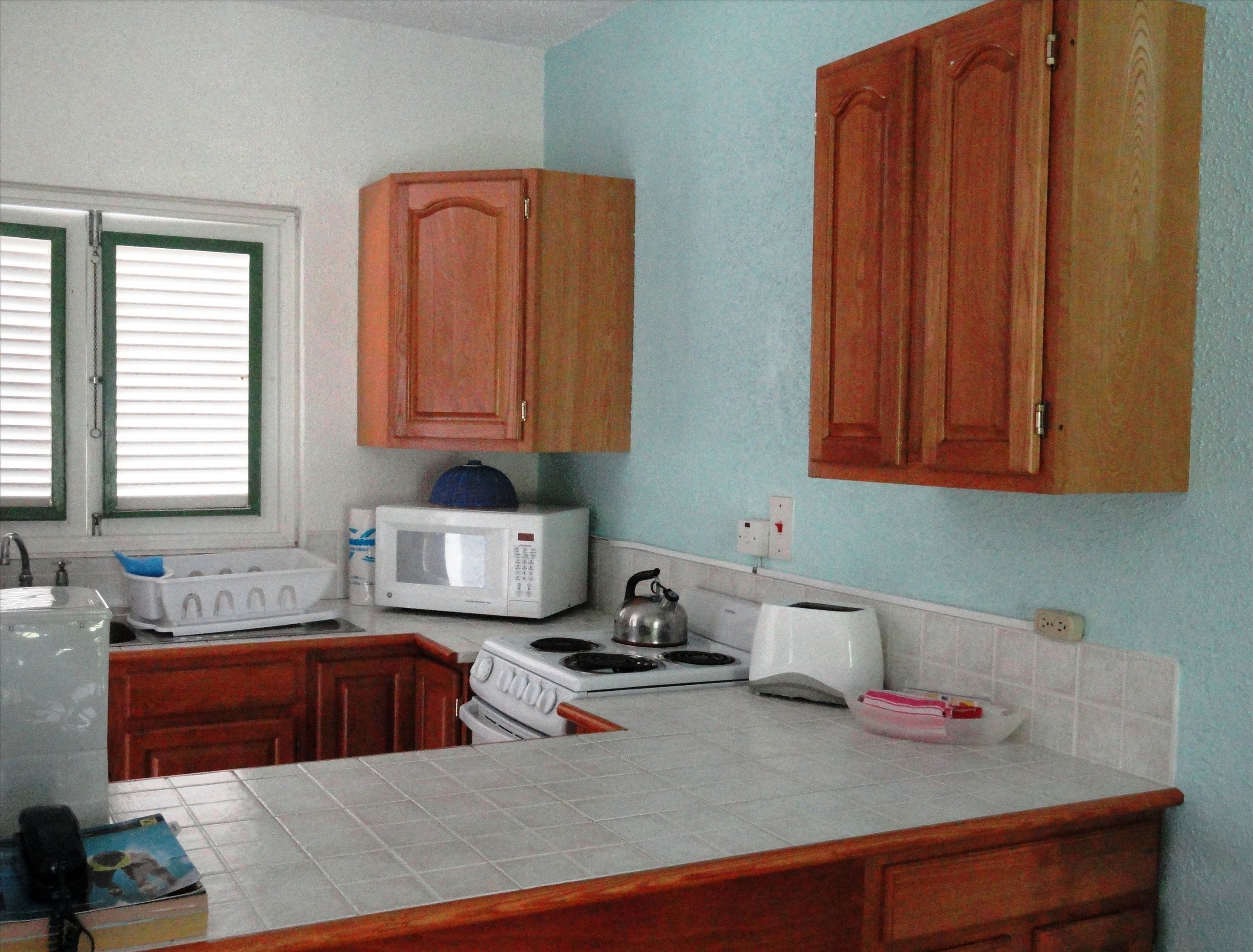 A kitchen with wooden cabinets, a microwave, a kettle, a toaster, and a sink.