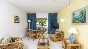 Una sala de estar con muebles de mimbre, una mesa de centro de vidrio y un televisor.