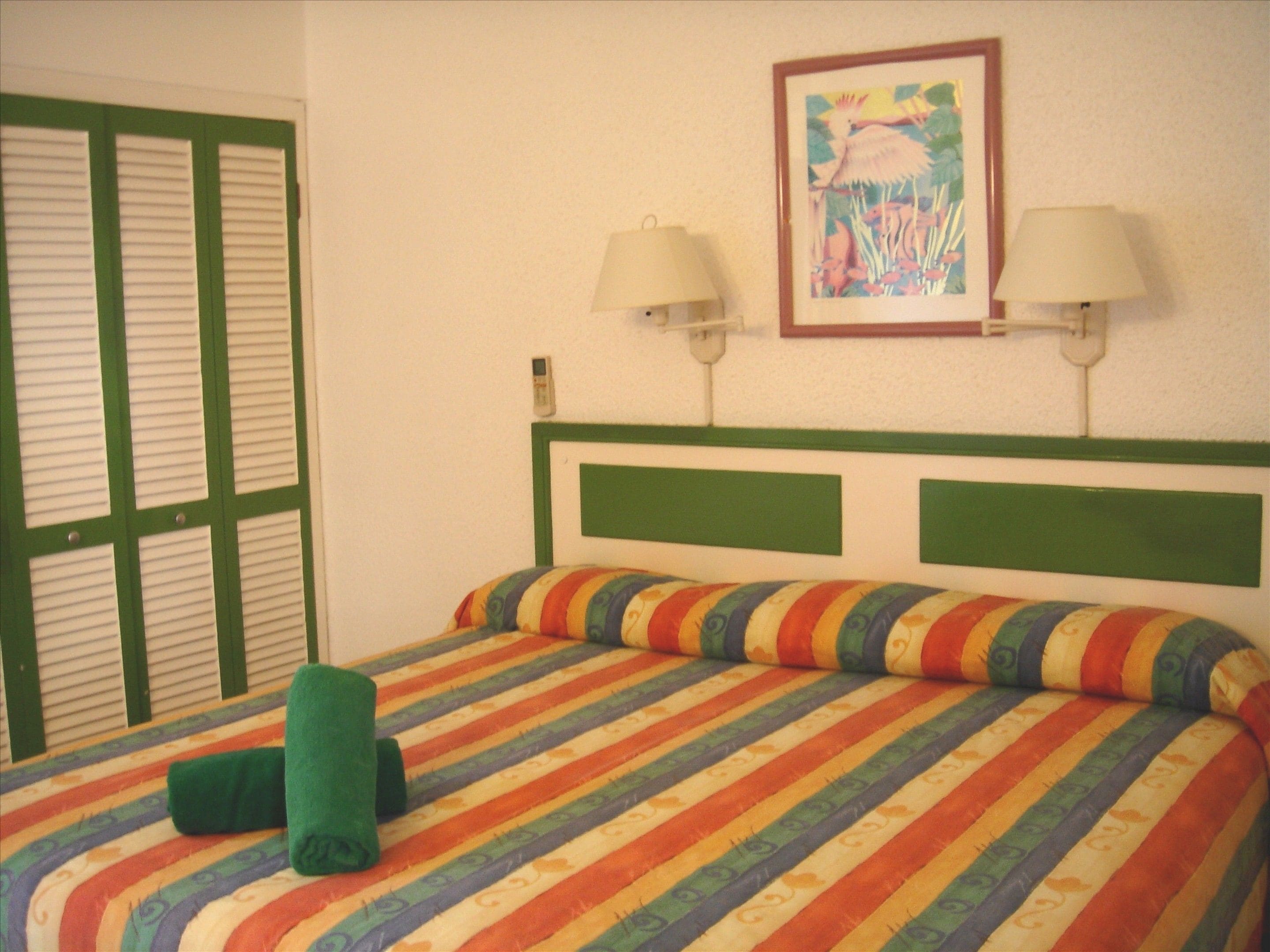 Habitación de hotel con edredón a rayas, dos lámparas de noche, un cuadro en la pared y una puerta verde.