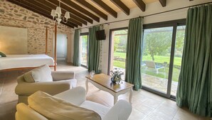 A spacious room with a bed, two white sofas, a wooden coffee table with a vase, and a view of a garden through large sliding glass doors. - Finca Hotel Son Pont (Puigpunyent)