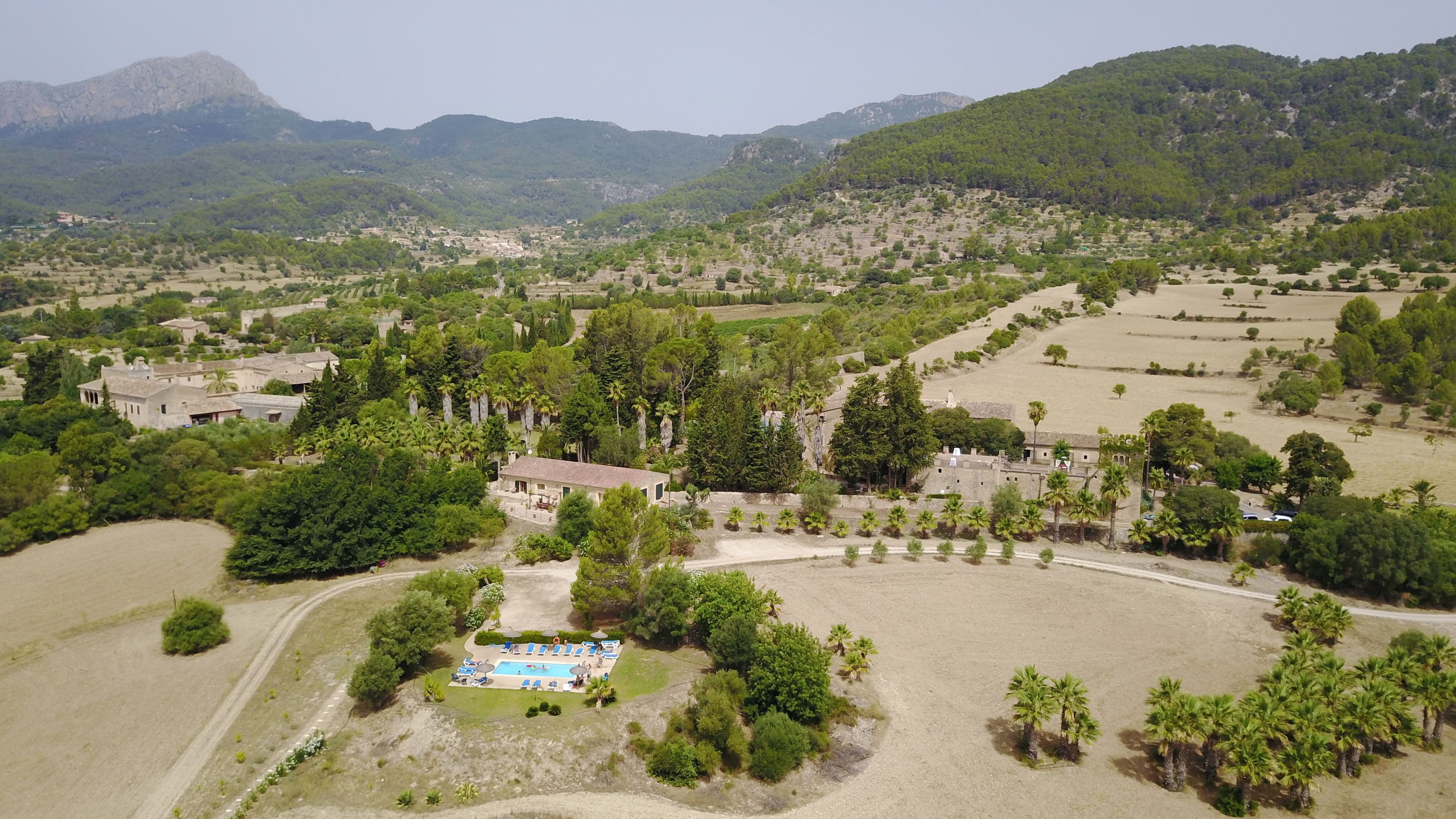 Une vue aérienne d’une zone rurale avec une piscine entourée d’arbres et de quelques bâtiments.