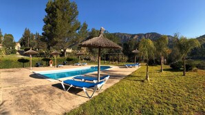 A swimming pool with lounge chairs and thatched umbrellas, surrounded by greenery and a mountain backdrop. - Finca Hotel Son Pont (Puigpunyent)