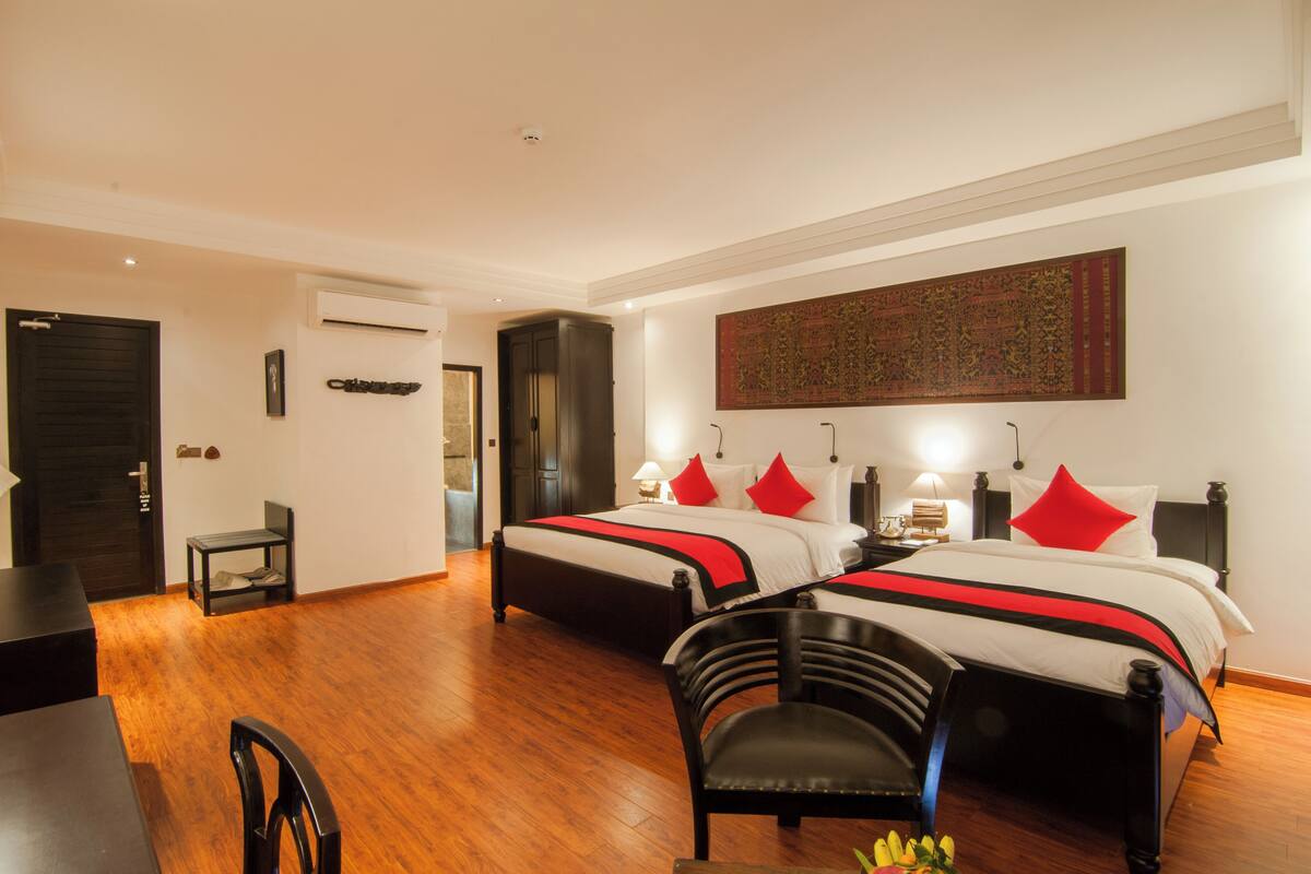 Habitación de hotel con dos camas, un escritorio, una silla y un tapiz decorativo grande.