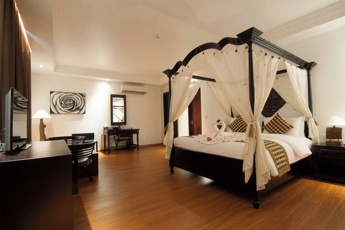 Una cama con dosel y cortinas, un escritorio con silla, un espejo y un televisor.