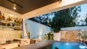 Zona de bar con piscina, pared de piedra y plantas en macetas.