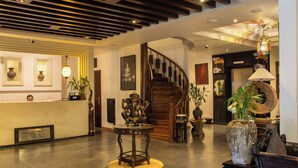 Un área de recepción con una escalera de madera, un mostrador de recepción y un jarrón grande con flores.