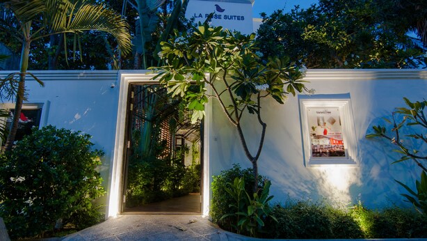 Un edificio blanco con un letrero que dice "LA ROSE SUITES" y una ventana que muestra el interior de una habitación.