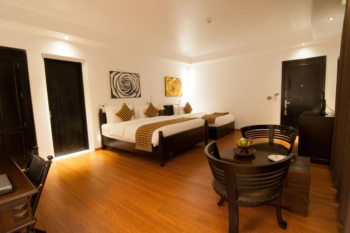 Una habitación de hotel con cama, mesitas de noche, una mesa de comedor con sillas y obras de arte en las paredes.