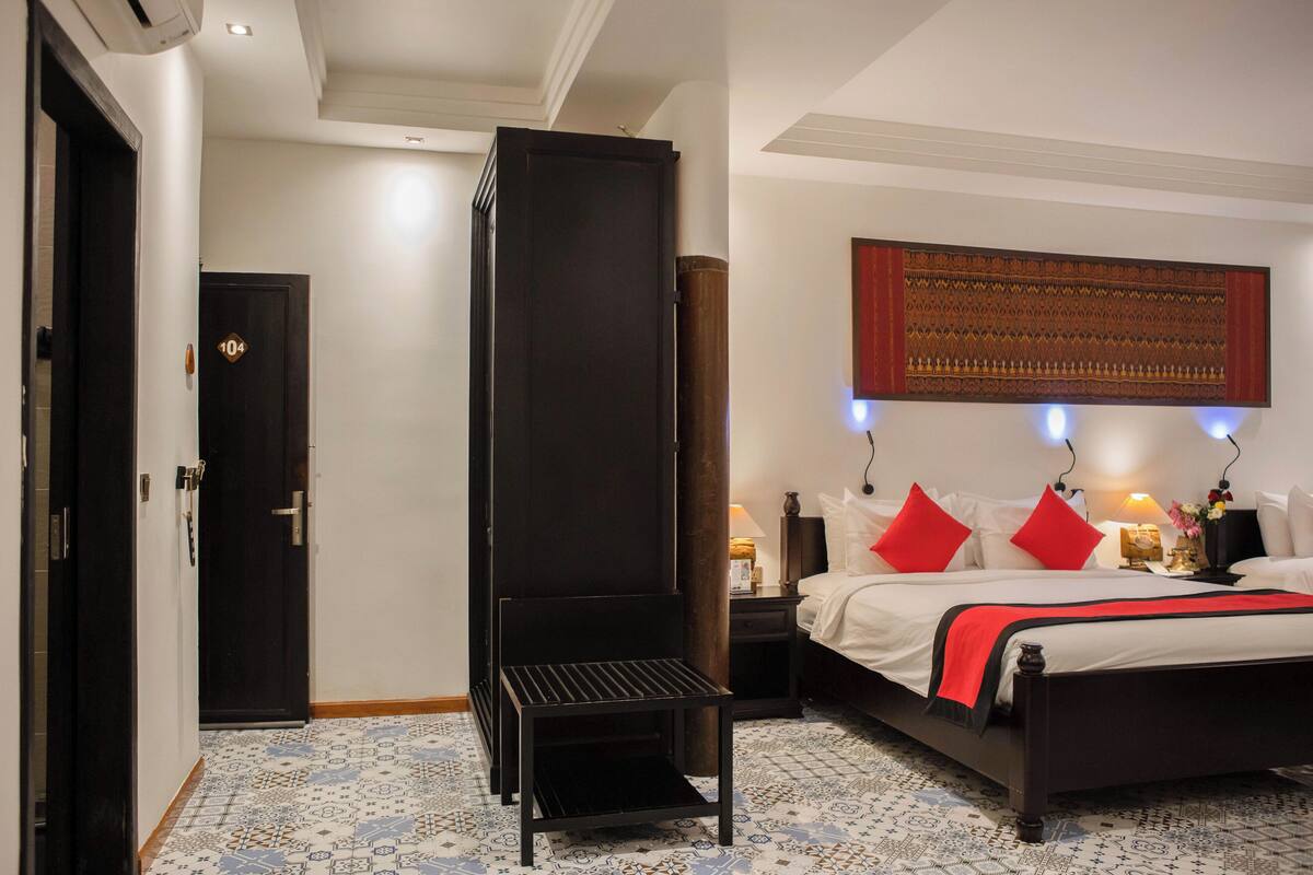 Una habitación de hotel con una cama, una mesita de noche, una lámpara, una obra de arte en la pared y un suelo con estampado.