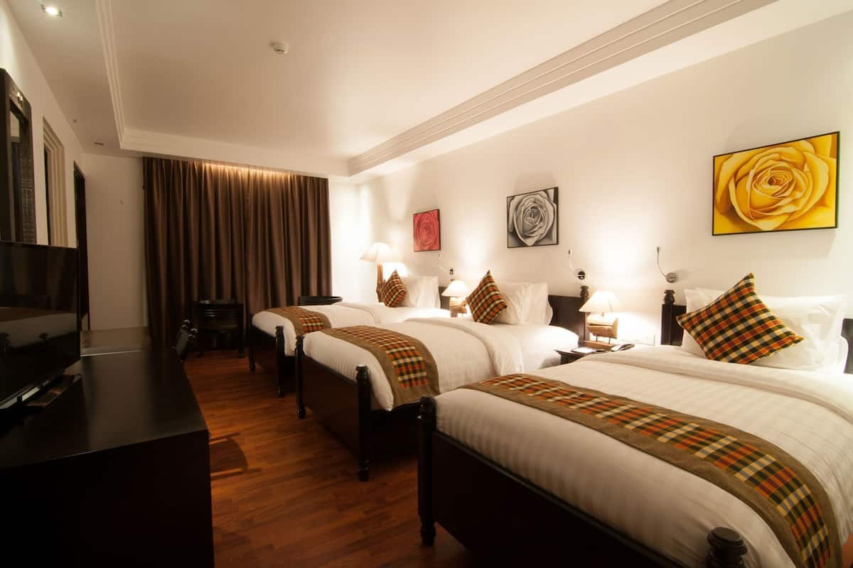 Una habitación de hotel con tres camas, televisión, escritorio y un ventanal grande con cortinas.