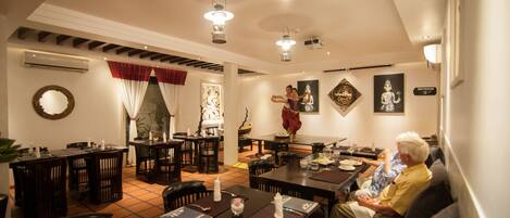 A dining area with multiple tables and chairs, an air conditioning unit, and a staircase leading to an upper level.
