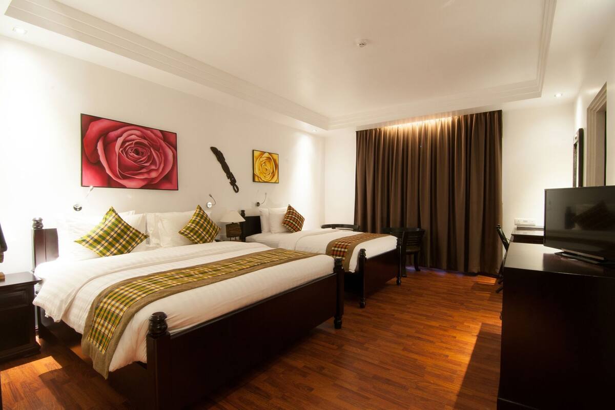 Habitación de hotel con dos camas, televisión, escritorio y un ventanal grande con cortinas.