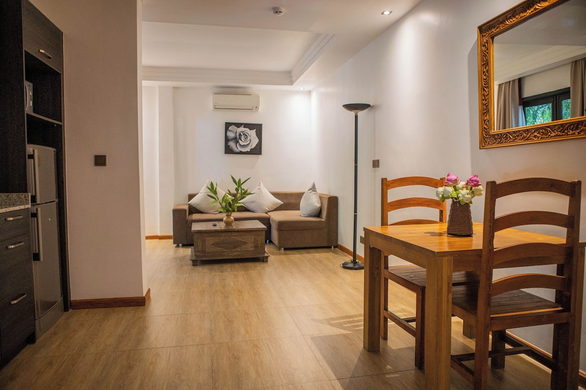 Una sala moderna con una mesa de comedor de madera, un sofá y una mesa de centro. Hay un refrigerador y una lámpara de pie en la habitación.