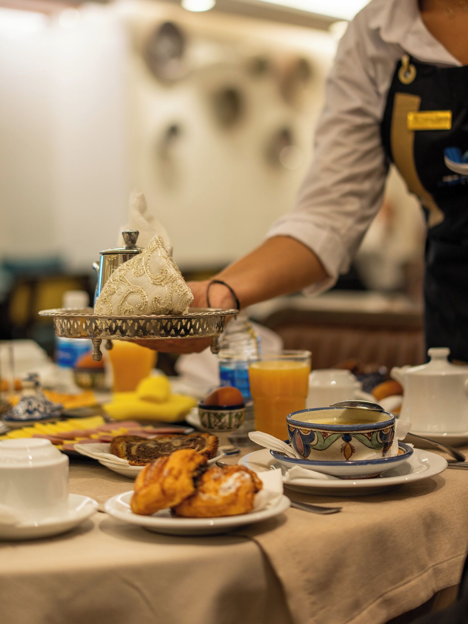 A breakfast buffet with various dishes, a coffee pot, and a person serving.