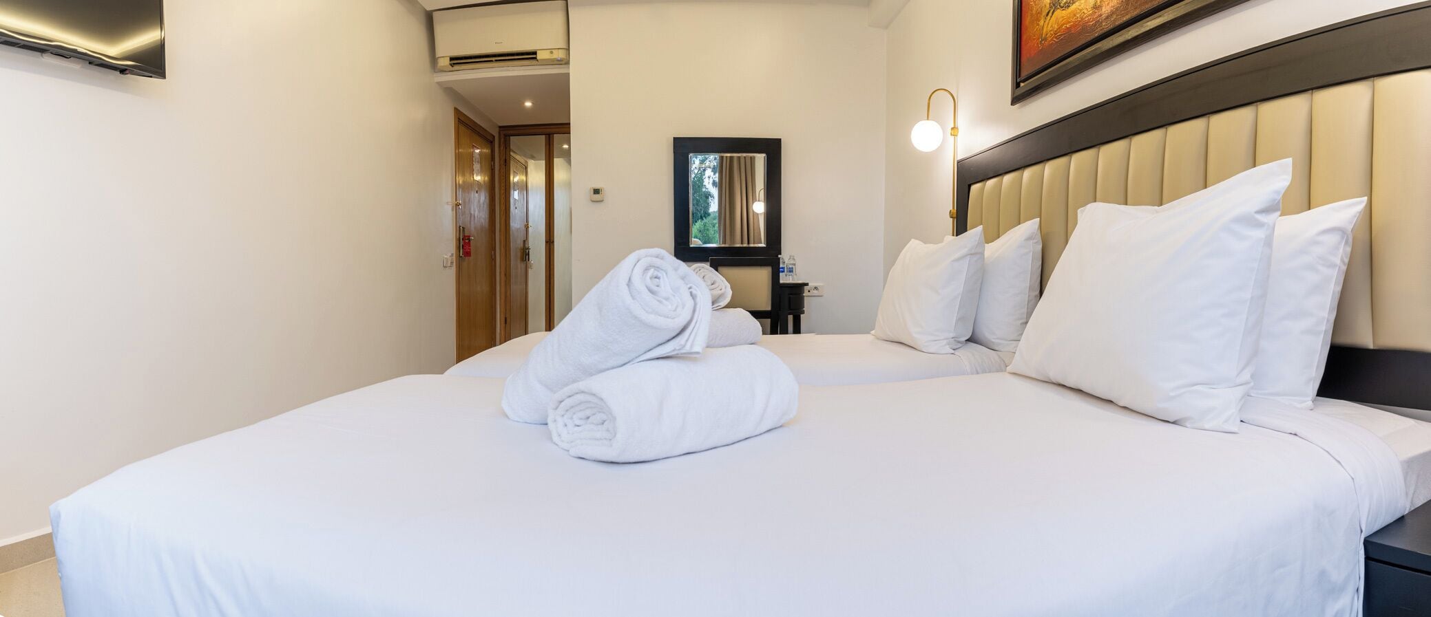 Une chambre d’hôtel avec deux lits, un miroir, un climatiseur fixé au mur et un tableau.