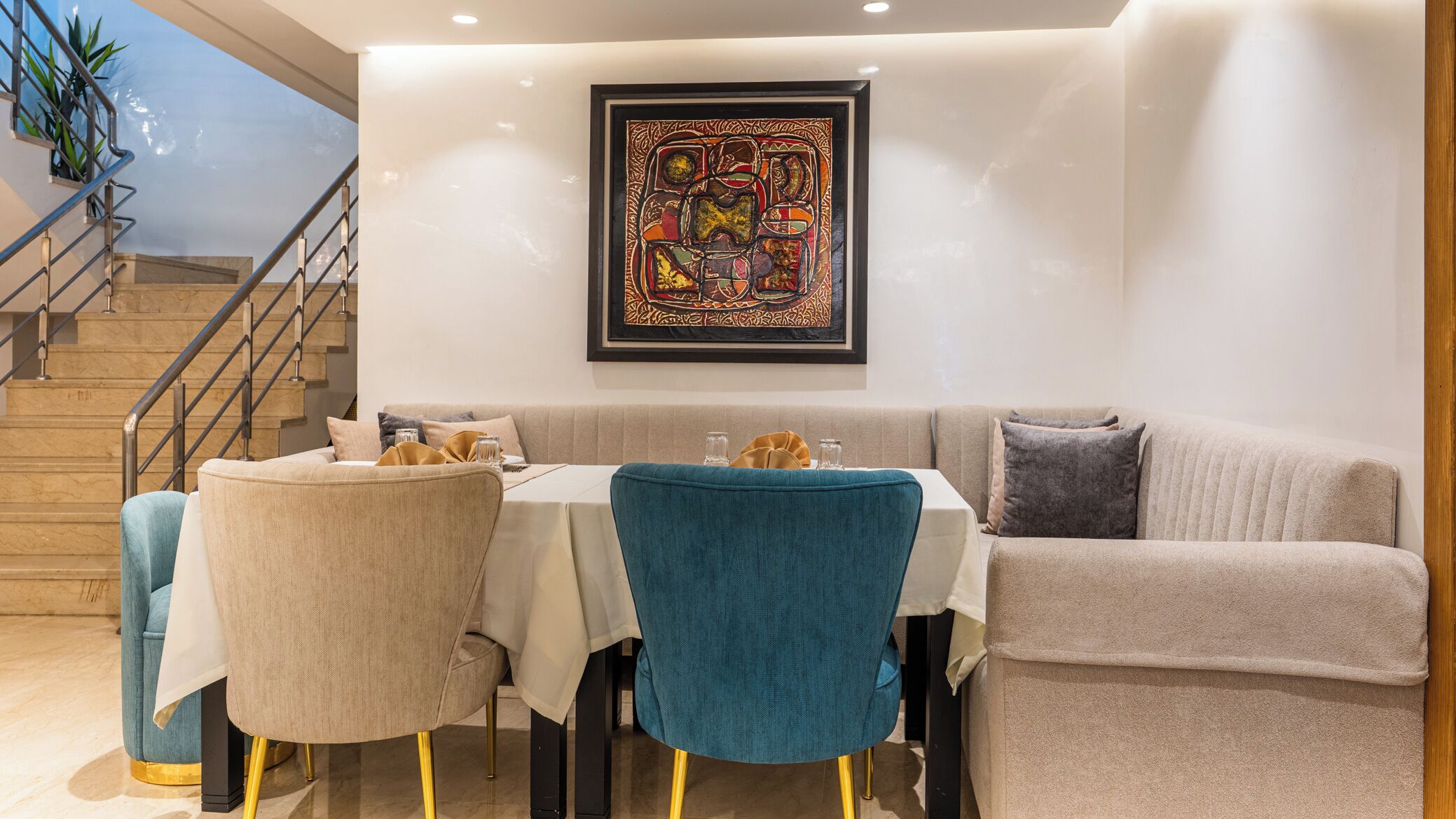 A dining area with a table set for two, a sofa, and a staircase.