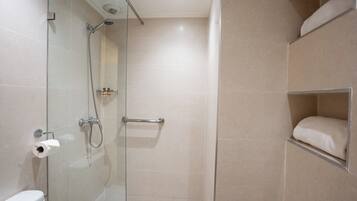Un baño con cabina de ducha de vidrio, inodoro y repisa con toalla.