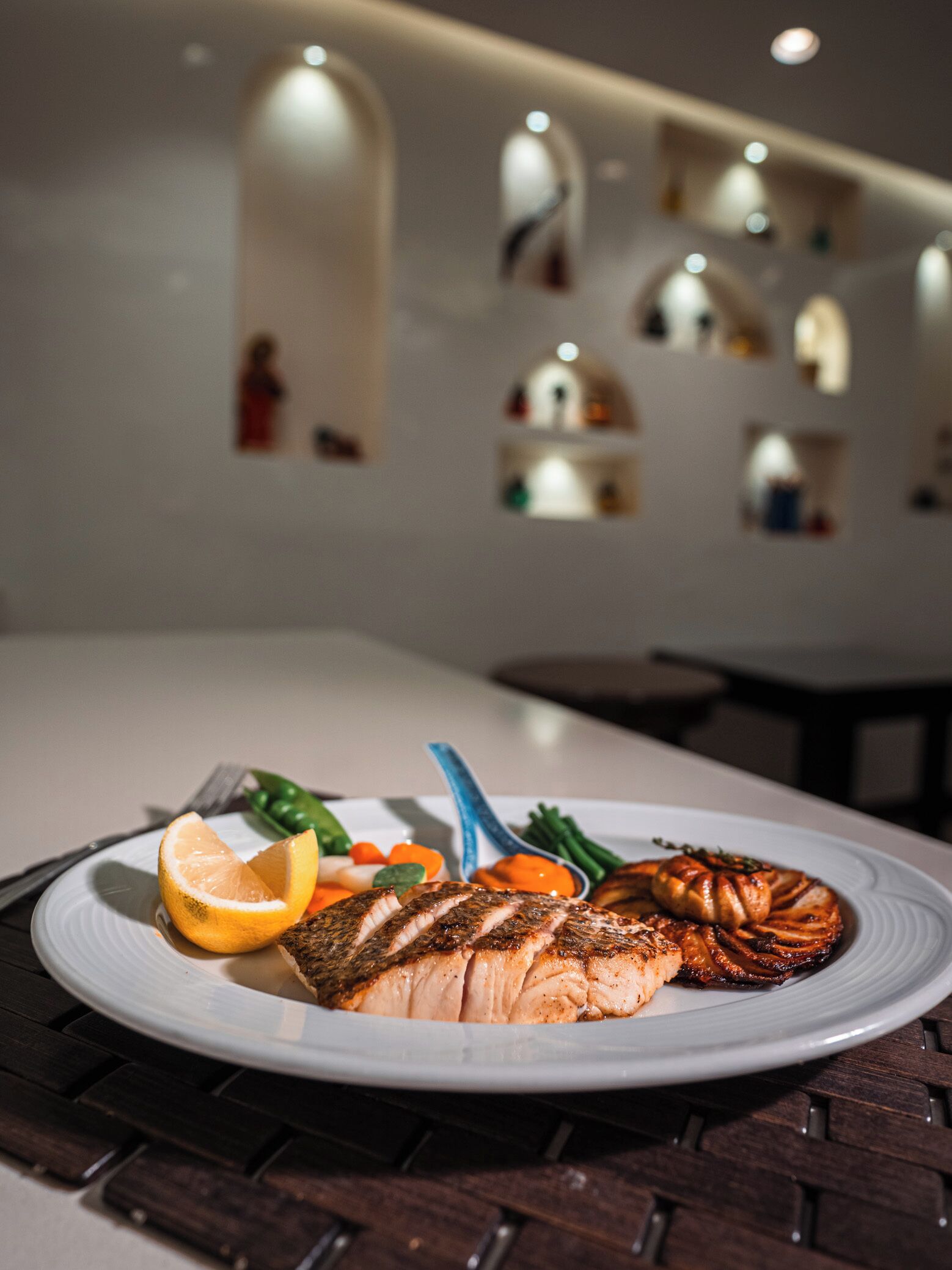 Een bord eten met een stuk zalm, een citroen en groenten op een tafel.