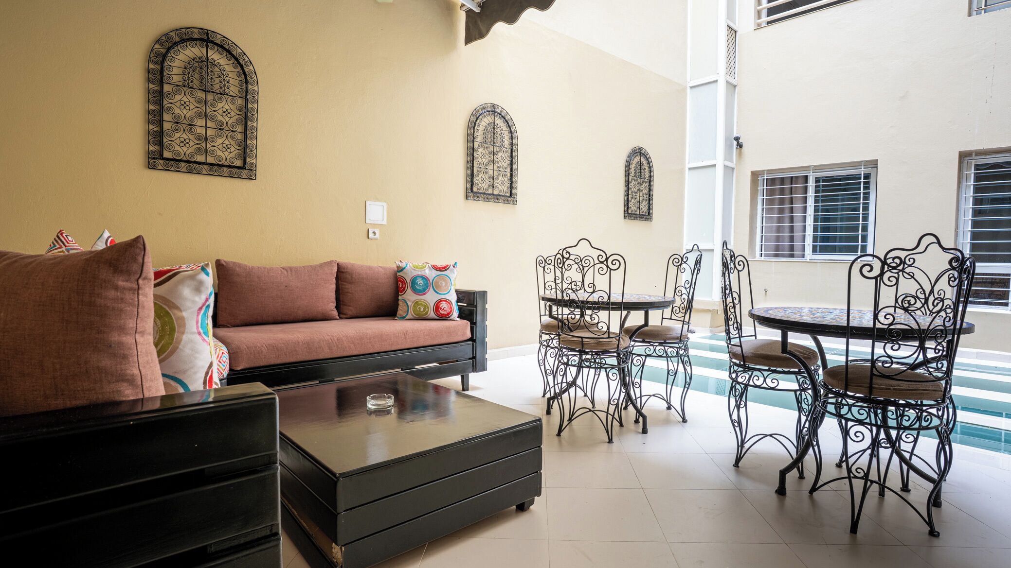 A living room with a sofa, coffee table, and metal chairs. There are decorative metal window grills on the walls.