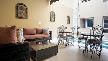A living room with a sofa, coffee table, and metal chairs. There are decorative metal window grills on the walls.