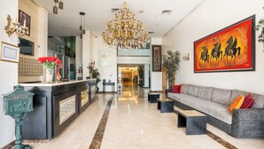 Un vestíbulo de hotel con mostrador de recepción, una araña y un sofá, además de un cuadro de gran tamaño.