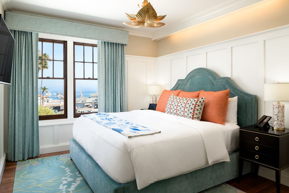 A neatly arranged bedroom with a large bed, a nightstand, and a view of the city through large windows.
