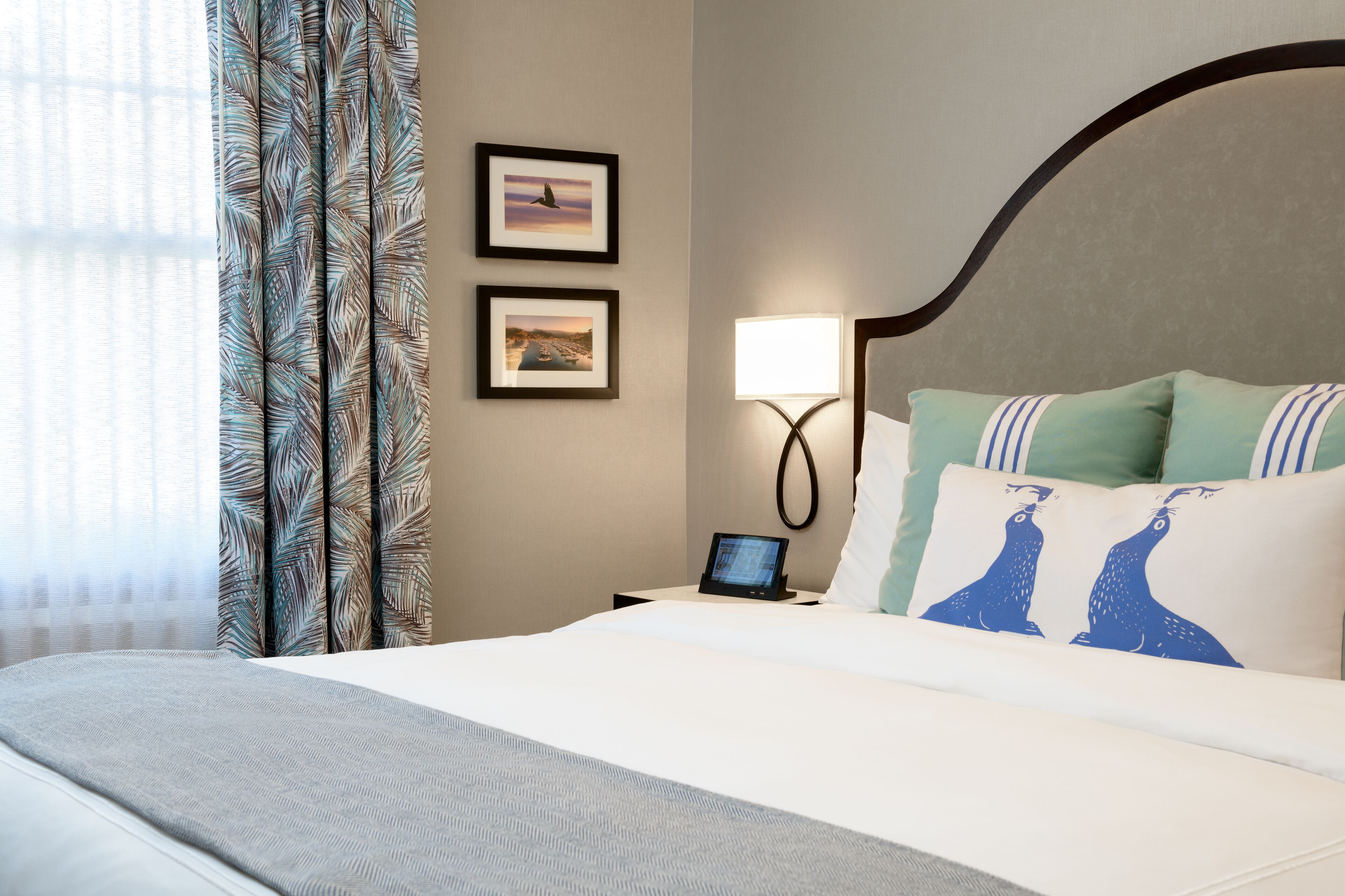 A hotel room with a bed, a nightstand with a lamp, and two framed pictures on the wall.