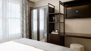 A hotel room with a bed, a wardrobe, a shelf with glasses and a bottle, and a small stool.