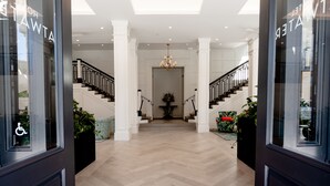 A spacious hallway with a herringbone floor, a chandelier, and a staircase with black railings. - Hotel Atwater (Avalon)