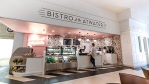 A bistro with a modern interior, featuring a counter with a menu, a display case with pastries, and a coffee machine. - Hotel Atwater (Avalon)