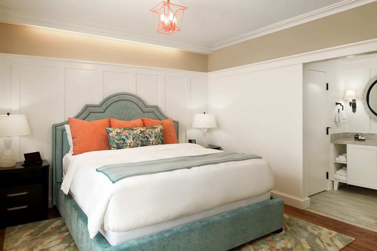 A neatly arranged bedroom with a bed, nightstands, a dresser, and a bathroom with a sink and mirror.