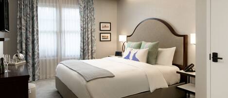A hotel room with a large bed, a desk, a chair, a lamp, and a television.