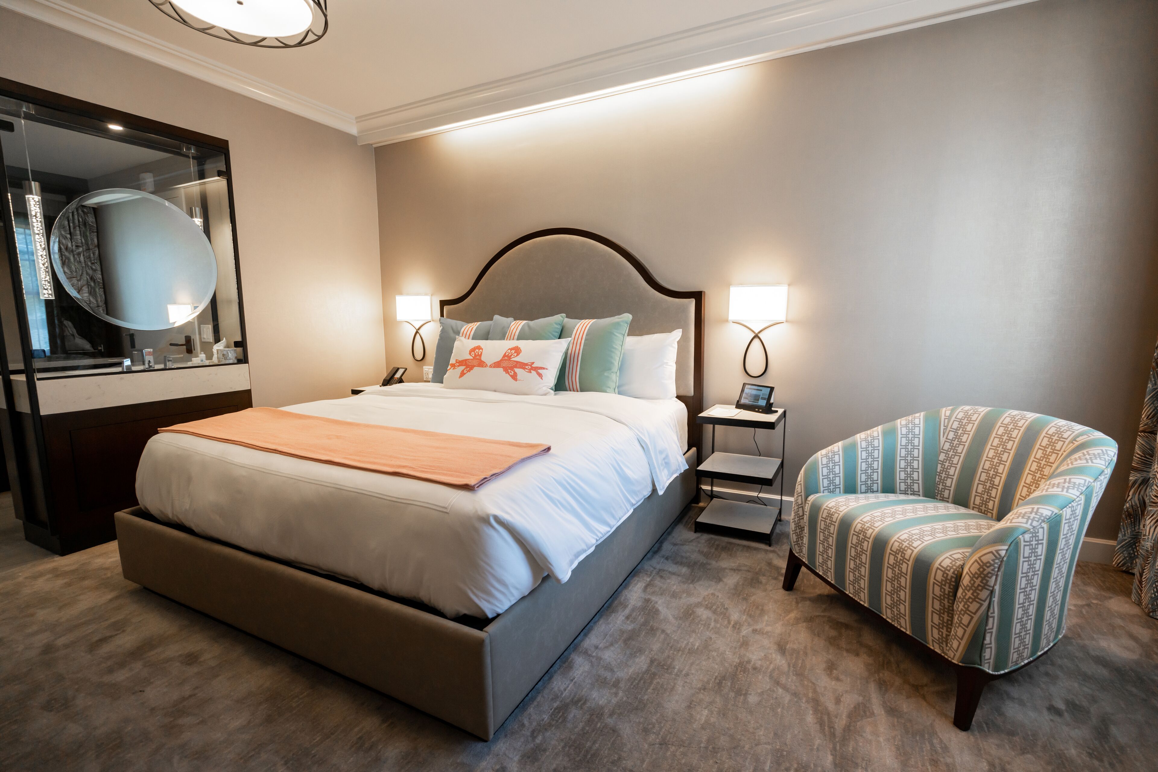 A hotel room with a large bed, a chair, a bedside table, a nightstand, a mirror, and a lamp.
