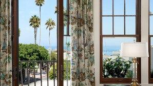 A room with a view of palm trees and the ocean through open French doors, a small table with a lamp, and a patterned rug. - Hotel Atwater (Avalon)