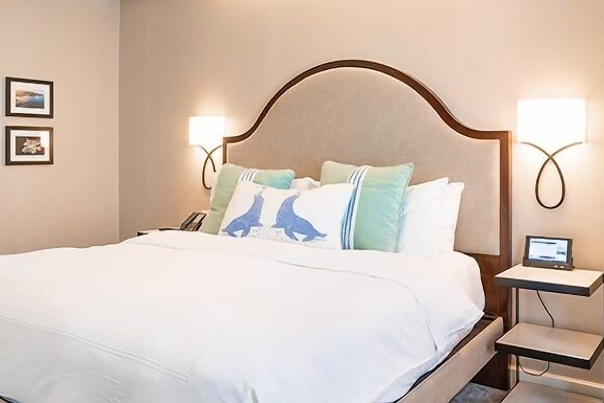 A hotel room with a large bed, a nightstand with a phone, and wall-mounted lights.