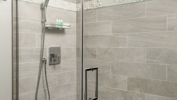 Ducha envuelta en vidrio con cabezal de ducha de mano y panel de control en la pared.