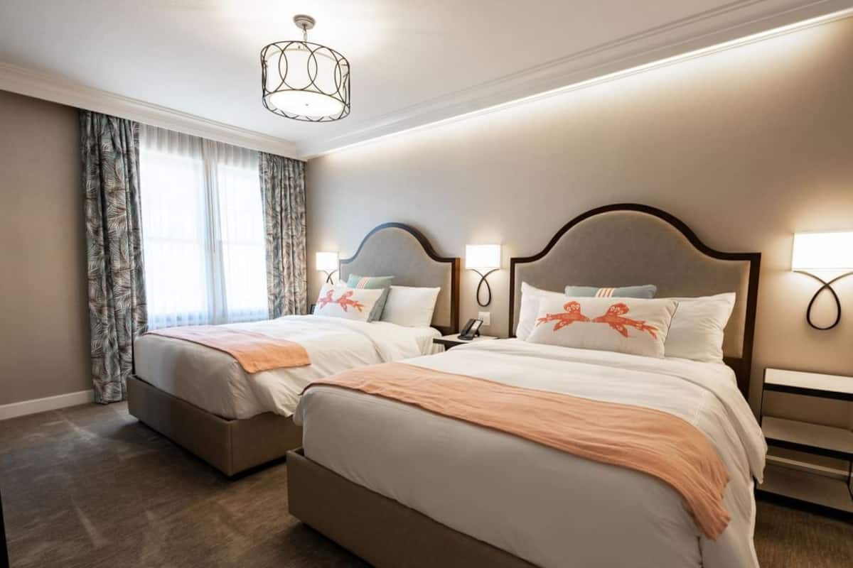 A hotel room with two beds, a chandelier, and a window with curtains.