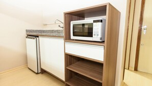 A compact kitchen with a microwave on a wooden shelf, a built-in refrigerator, and a countertop with a sink. - Letto Hotel Porto Alegre (Porto Alegre)