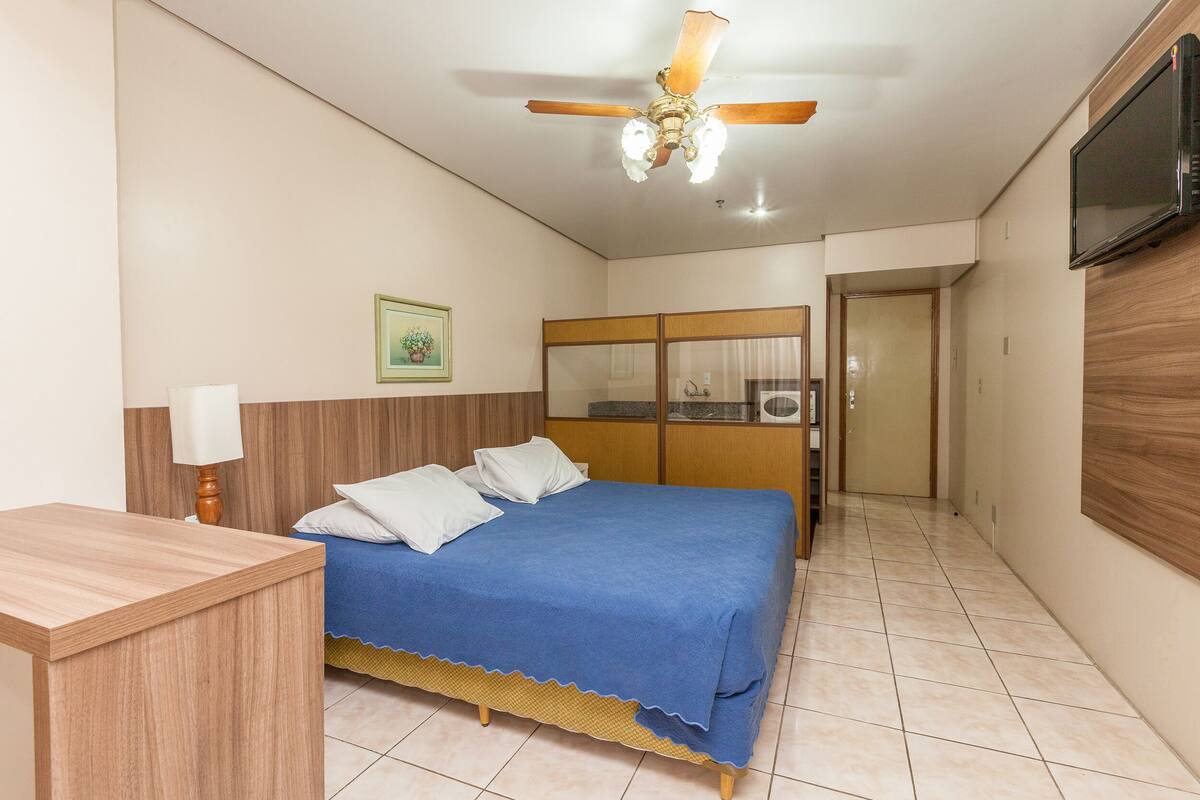 Un dormitorio con cama, escritorio, ventilador de techo, televisor y armario.